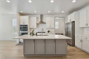 Kitchen with stainless steel appliances, white cabinets, wall chimney exhaust hood, recessed lighting, and a center island with sink