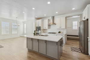 Kitchen featuring appliances with stainless steel finishes, light wood-type flooring, white cabinetry, wall chimney range hood, and recessed lighting