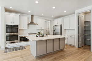 Kitchen with recessed lighting, a center island with sink, wall chimney range hood, stainless steel appliances, with walk in pantry.