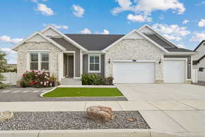 View of front of house with stucco and  stone siding, an attached garage & driveway,