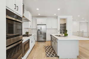 Kitchen featuring appliances with stainless steel finishes, light wood-style flooring, recessed lighting, white cabinetry, and wall chimney exhaust hood