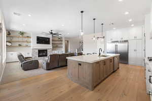 Kitchen with pendant lighting, white cabinetry, open floor plan, stainless steel built in fridge, and a stone fireplace