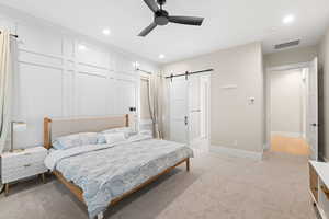 Bedroom with a barn door, light colored carpet, ceiling fan, and recessed lighting