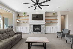 Living area featuring a stone fireplace, light colored carpet, recessed lighting, and a ceiling fan