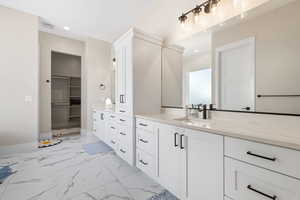 Full bathroom with vanity, a spacious closet, light marble finish floors, and recessed lighting