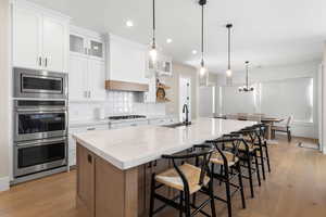 Kitchen with glass insert cabinets, a kitchen bar, white cabinetry, light stone counters, and a kitchen island with sink