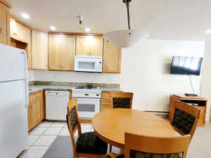 Kitchen featuring recessed lighting, white appliances, light brown cabinetry, hanging light fixtures, and light stone countertops