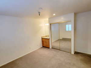 Unfurnished bedroom featuring light carpet, a closet, ensuite bathroom, recessed lighting, and a baseboard heating unit