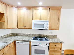 Kitchen featuring white appliances, light brown cabinets, and light stone counters