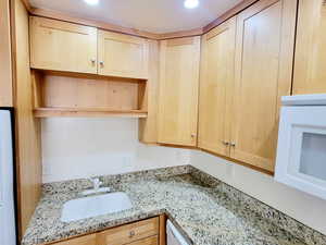Kitchen with light stone countertops, white appliances, light brown cabinetry, and open shelves