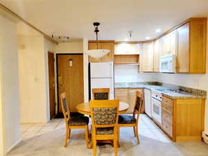 Kitchen featuring decorative light fixtures, white appliances, light tile patterned floors, recessed lighting, and light stone countertops