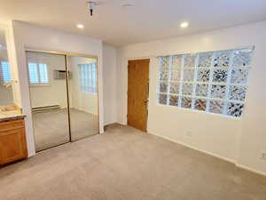 Unfurnished bedroom with light carpet, a closet, baseboard heating, and recessed lighting