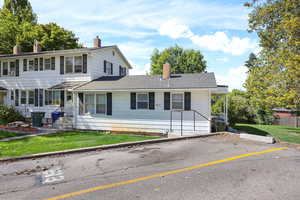 View of front of home featuring a front lawn, a shingled roof, a chimney, and uncovered parking
