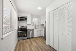 Kitchen featuring white cabinetry, stainless steel appliances, tasteful backsplash, and light wood-style floors