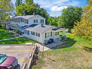 Rear view of house with a chimney, a shingled roof, a yard, and uncovered parking