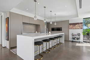 Kitchen with modern cabinets, gray cabinets, a kitchen bar, decorative light fixtures, and finished concrete flooring