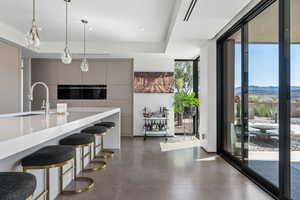 Kitchen with a wall of windows, hanging light fixtures, modern cabinets, concrete flooring, and a kitchen bar