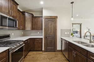 Kitchen with stainless steel appliances, hanging light fixtures, dark brown cabinets, backsplash, and recessed lighting