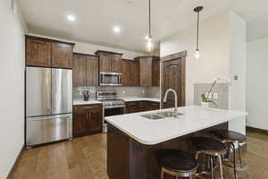 Kitchen with appliances with stainless steel finishes, tasteful backsplash, dark wood-style floors, hanging light fixtures, and dark brown cabinetry