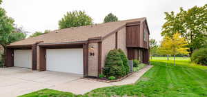 View of home's exterior with brick siding, a yard, roof with shingles, a garage, and concrete driveway