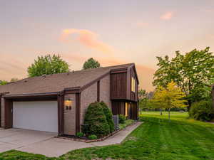 Mid-century modern home featuring a lawn, brick siding, a garage, driveway, and roof with shingles