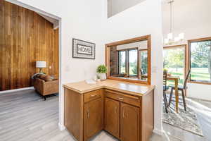 Kitchen with brown cabinets, wooden walls, light countertops, light wood-style flooring, and hanging light fixtures