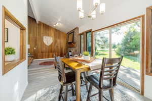 Dining space featuring vaulted ceiling, wood walls, light wood-style floors, and a chandelier