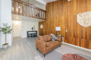 Living area featuring a towering ceiling, wood finished floors, wood walls, beam ceiling, and ceiling fan
