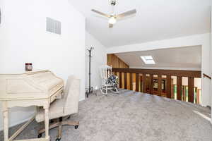 Carpeted home office featuring lofted ceiling, a skylight, and a ceiling fan