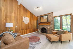 Living area featuring a fireplace, wood finished floors, wood walls, and high vaulted ceiling