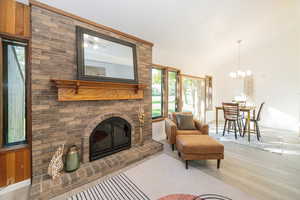 Living area featuring a brick fireplace, wood finished floors, a chandelier, and high vaulted ceiling