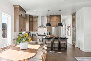 Kitchen featuring tasteful backsplash, a kitchen bar, high quality appliances, hanging light fixtures, and wall chimney range hood