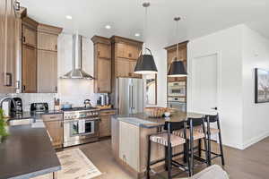 Kitchen with backsplash, wall chimney exhaust hood, high quality appliances, dark wood-type flooring, and recessed lighting