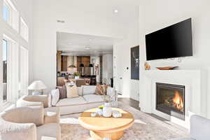 Living area featuring recessed lighting, a glass covered fireplace, wood finished floors, healthy amount of natural light, and a towering ceiling