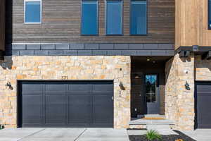 Entrance to property with an attached garage, concrete driveway, and stone siding