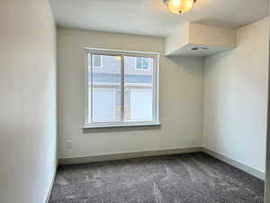 Spare room featuring dark colored carpet and baseboards