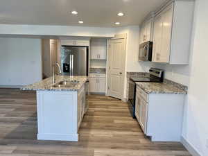 Kitchen featuring light stone counters, stainless steel appliances, recessed lighting, a kitchen island with sink, and light wood-style flooring