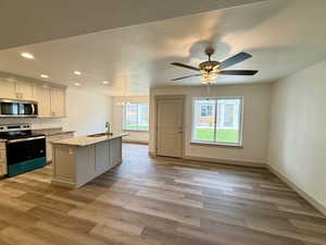 Kitchen featuring stainless steel appliances, a chandelier, a center island with sink, light stone countertops, and recessed lighting