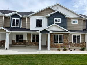 View of front of house featuring a front yard, stone siding, board and batten siding, and roof with shingles