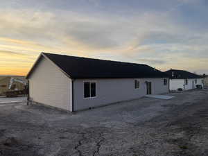 Back of property at dusk with a shingled roof and a patio area