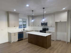 Kitchen with stainless steel appliances, a center island, decorative light fixtures, dark wood-style flooring, and light stone countertops