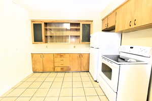Kitchen with white appliances, open shelves, light countertops, light tile patterned flooring, and light brown cabinetry
