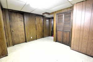 Finished below grade area featuring wood walls, a paneled ceiling, and light flooring