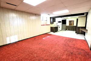 Basement with a paneled ceiling, wooden walls, and light carpet