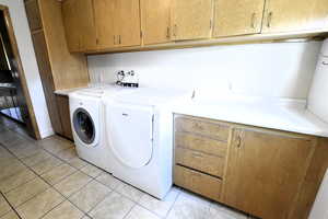 Washroom featuring independent washer and dryer, light tile patterned floors, and cabinet space
