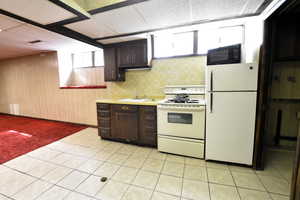 Kitchen with dark brown cabinets, white appliances, light countertops, light tile patterned flooring, and a paneled ceiling