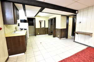 Kitchen featuring light tile patterned floors, dark brown cabinetry, light countertops, wooden walls, and white electric range