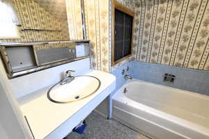 Bathroom with a bath, vanity, and wallpapered walls