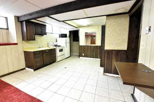 Kitchen featuring wooden walls, light countertops, light tile patterned floors, dark brown cabinets, and white appliances