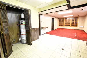 Finished basement with a drop ceiling, wood walls, water heater, and light tile patterned flooring